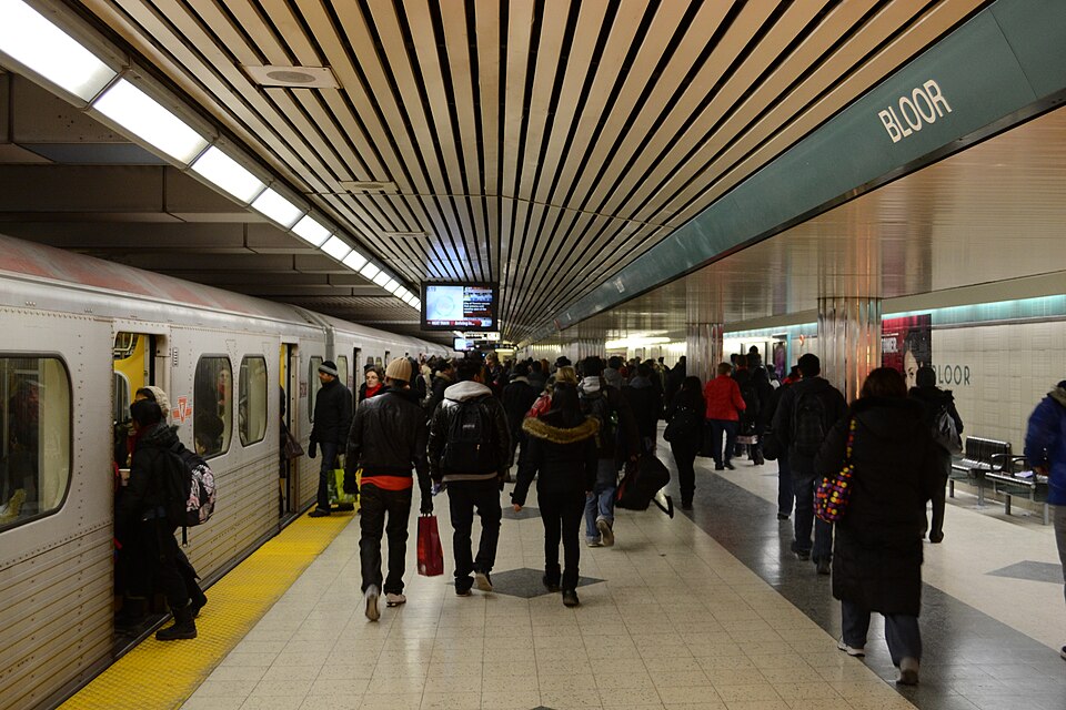 Another subway train stopped at a very crowded, busy station platform. Many people are boarding the train.